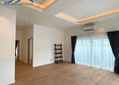 Modern living room with wooden floors, recess lighting, and large windows with curtains