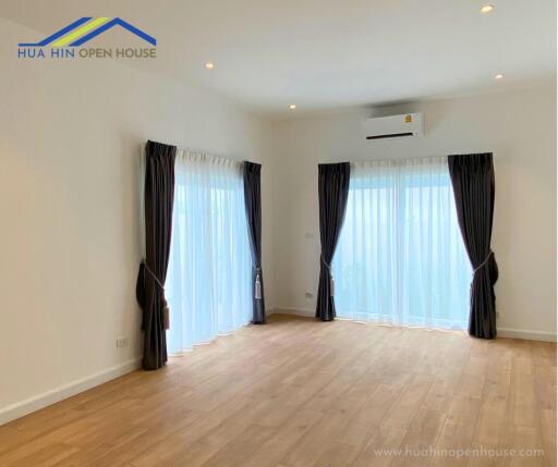 Spacious living room with wood flooring, large windows, and ceiling lights.