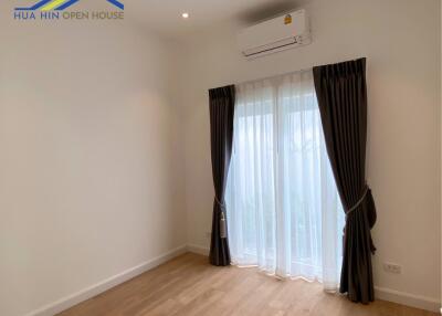 Empty bedroom with wooden flooring, curtains, and air conditioning