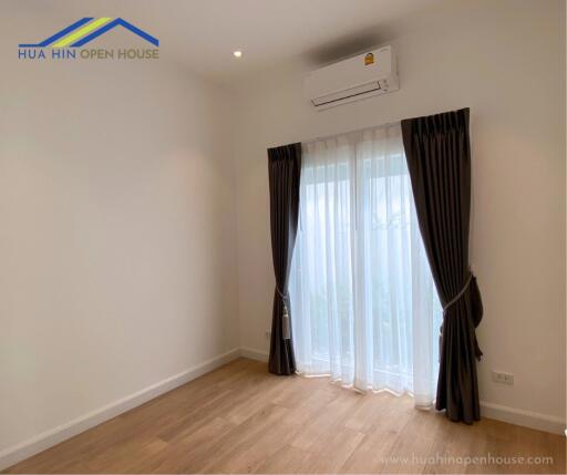 Empty bedroom with wooden flooring, curtains, and air conditioning