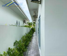 Narrow outdoor walkway beside a modern building with white walls and green plants