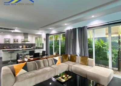 Modern living room with a large L-shaped sofa, adjoining kitchen and dining area in an open-plan layout.