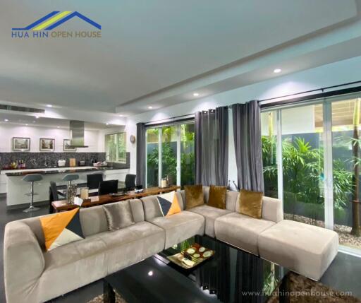 Modern living room with a large L-shaped sofa, adjoining kitchen and dining area in an open-plan layout.