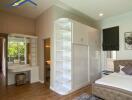 A well-lit bedroom with a large white wardrobe, vanity area, and a bed with tufted headboard