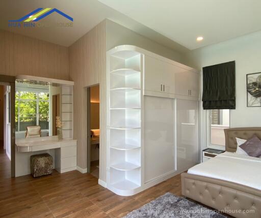 A well-lit bedroom with a large white wardrobe, vanity area, and a bed with tufted headboard