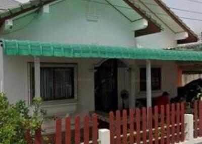 Front view of a small house with green roofing and a red fence