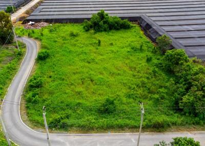 Aerial view of a vacant green land plot surrounded by a road and covered areas