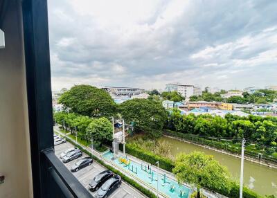 View from the balcony overlooking a parking area, green trees, a river, and distant buildings under a cloudy sky.