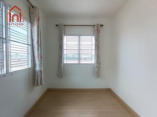 Small empty bedroom with wooden floor, two windows with curtains, and white walls