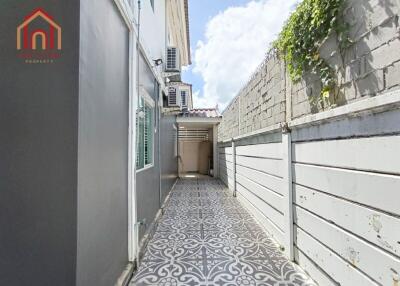 Narrow outdoor pathway with decorative patterned tiles and a wall with greenery