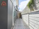 Narrow outdoor pathway with decorative patterned tiles and a wall with greenery