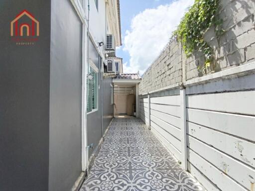 Narrow outdoor pathway with decorative patterned tiles and a wall with greenery