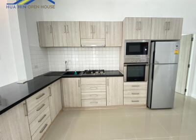 Modern kitchen with wooden cabinets, black countertops, and stainless steel appliances.