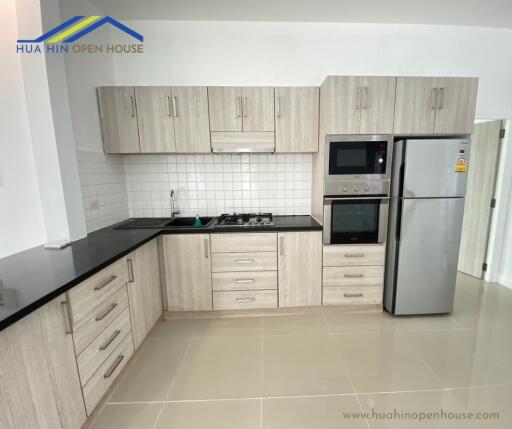 Modern kitchen with wooden cabinets, black countertops, and stainless steel appliances.