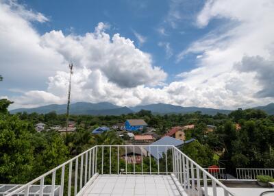 View from rooftop terrace overlooking trees, houses, and mountains under a partly cloudy sky