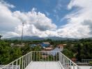 View from rooftop terrace overlooking trees, houses, and mountains under a partly cloudy sky