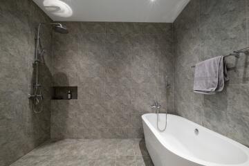 Modern bathroom with grey tiled walls and flooring, a freestanding bathtub, and a shower