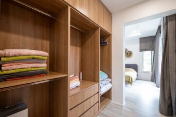 A spacious walk-in closet with wooden cabinetry, open shelving, and drawers, leading to a bedroom.