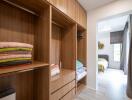 A spacious walk-in closet with wooden cabinetry, open shelving, and drawers, leading to a bedroom.