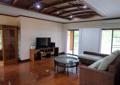 Spacious living room with wooden flooring, modern ceiling design, large windows, and comfortable seating