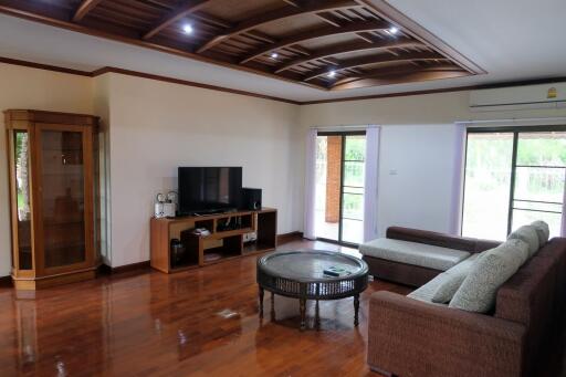 Spacious living room with wooden flooring, modern ceiling design, large windows, and comfortable seating