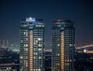 Night view of two high-rise residential buildings with city lights in the background