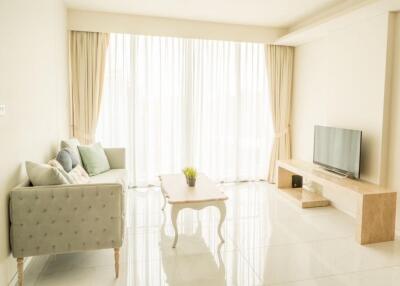 A bright and spacious living room with a large window, light-colored sofa, coffee table, and TV on a wooden stand.