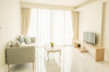 A bright and spacious living room with a large window, light-colored sofa, coffee table, and TV on a wooden stand.