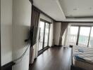 Modern bedroom with large windows, dark hardwood floor, and wall-mounted TV