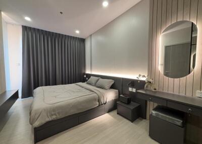 Modern bedroom with double bed, nightstands, and a vanity under warm lighting.