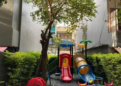 Outdoor playground with colorful play structures, including slides and climbing equipment, surrounded by greenery and secure fencing