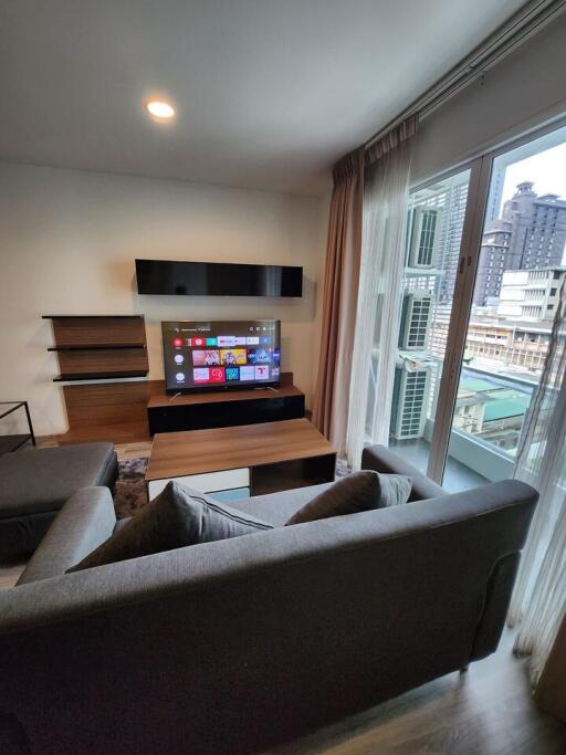 Modern living room with a large window, sectional sofa, TV, and shelves