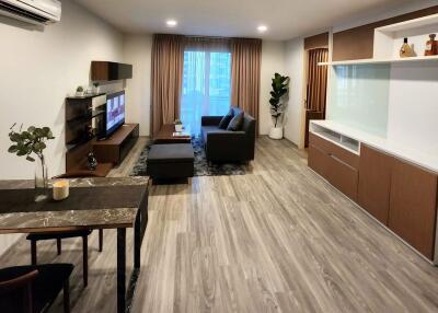 Modern living room with wooden flooring, couch, TV, and dining area