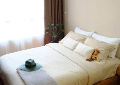 Cozy bedroom with a bed, pillows, stuffed toy, and plant near a large window