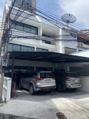 Front view of a multi-story building with multiple parked cars and rooftop satellite dish