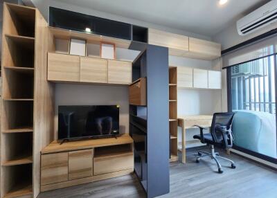 Modern living area with built-in wooden cabinets, TV, desk, and sliding glass door