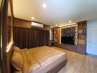 Modern bedroom with large bed, TV, wooden floor, and built-in shelves