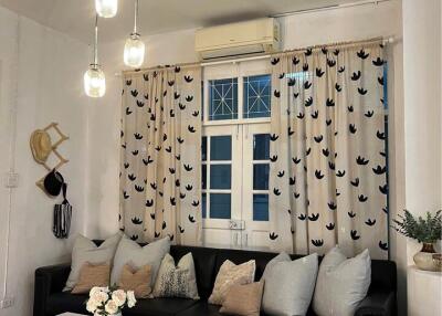 Cozy living room with black leather sofa and decorative cushions, decorated with hanging lights and floral arrangements