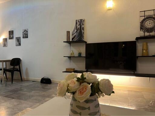 A beautifully decorated living room with a wall-mounted TV, shelves, wall art, and a vase of flowers on the coffee table