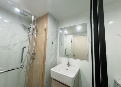 Modern bathroom with marble walls, wall-mounted sink, large mirror, and shower area