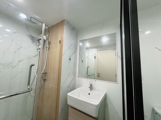 Modern bathroom with marble walls, wall-mounted sink, large mirror, and shower area