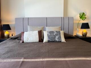 Modern bedroom with large bed and decorative pillows, featuring nightstands with lamps and plant decor