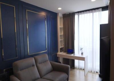 Modern living room with blue accent wall and a desk near windows with white curtains