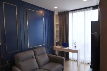 Modern living room with blue accent wall and a desk near windows with white curtains