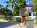 Private resort exterior with tropical trees, a thatched entrance gate, and a 'For Sale' sign