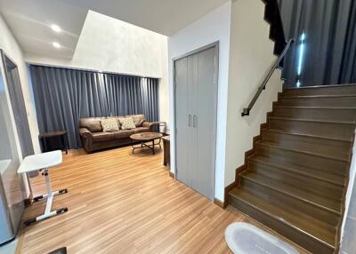 Living room with a brown couch, coffee table, stairs leading up, and wood flooring