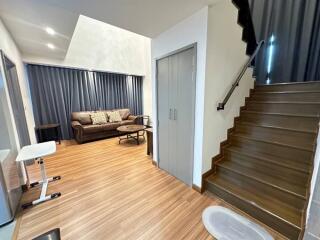 Living room with a brown couch, coffee table, stairs leading up, and wood flooring