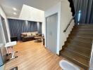 Living room with a brown couch, coffee table, stairs leading up, and wood flooring