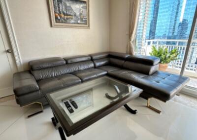 Modern living room with leather sectional sofa and glass coffee table next to a large window