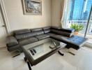 Modern living room with leather sectional sofa and glass coffee table next to a large window